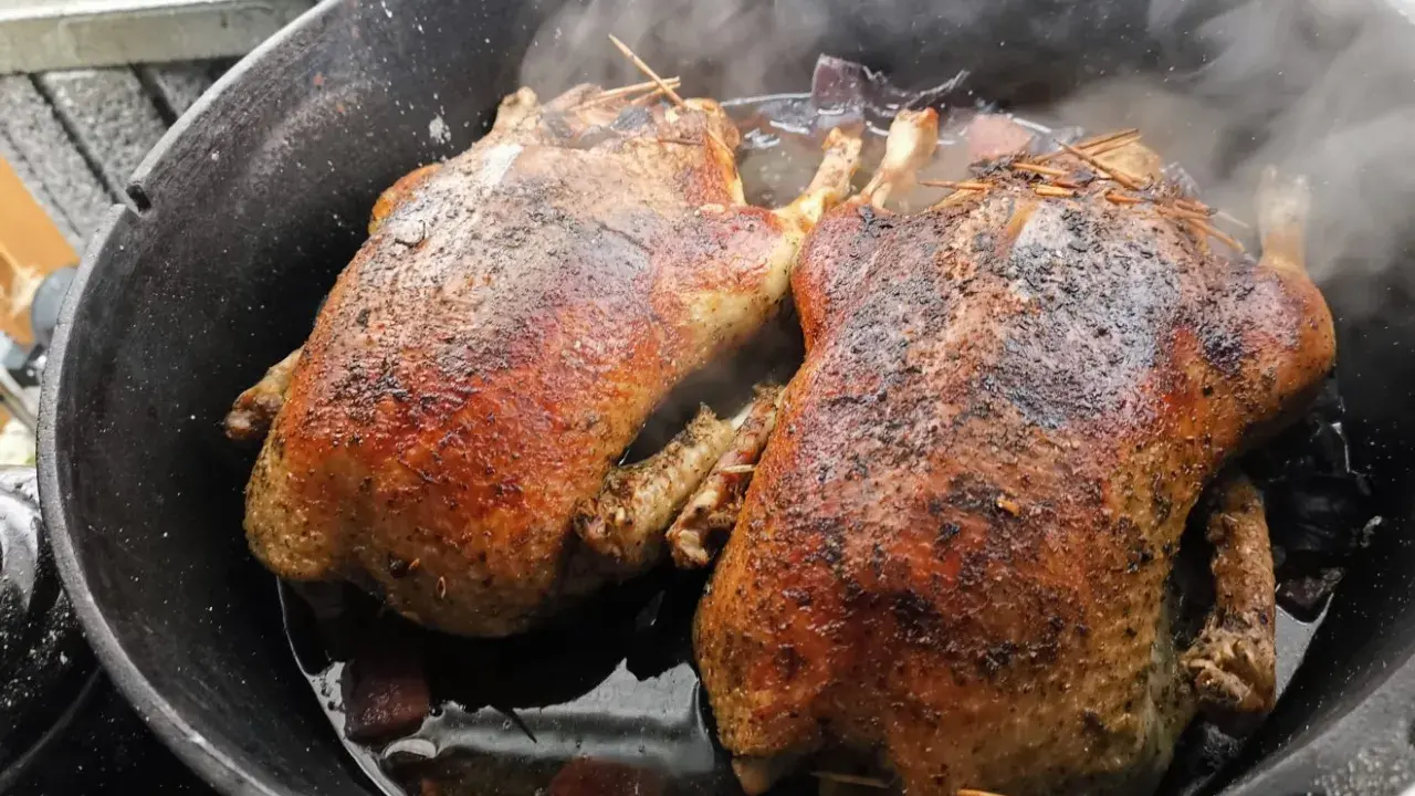 Zwei goldbraune Enten garen im Dutch Oven. Dampf steigt auf, während die Enten im eigenen Saft schmoren.
