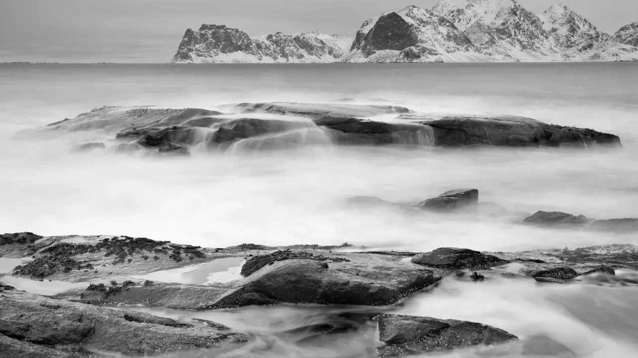 Vatten virvlar runt stenar vid en snötäckt kust. Perfekt för zoom fotoresor.