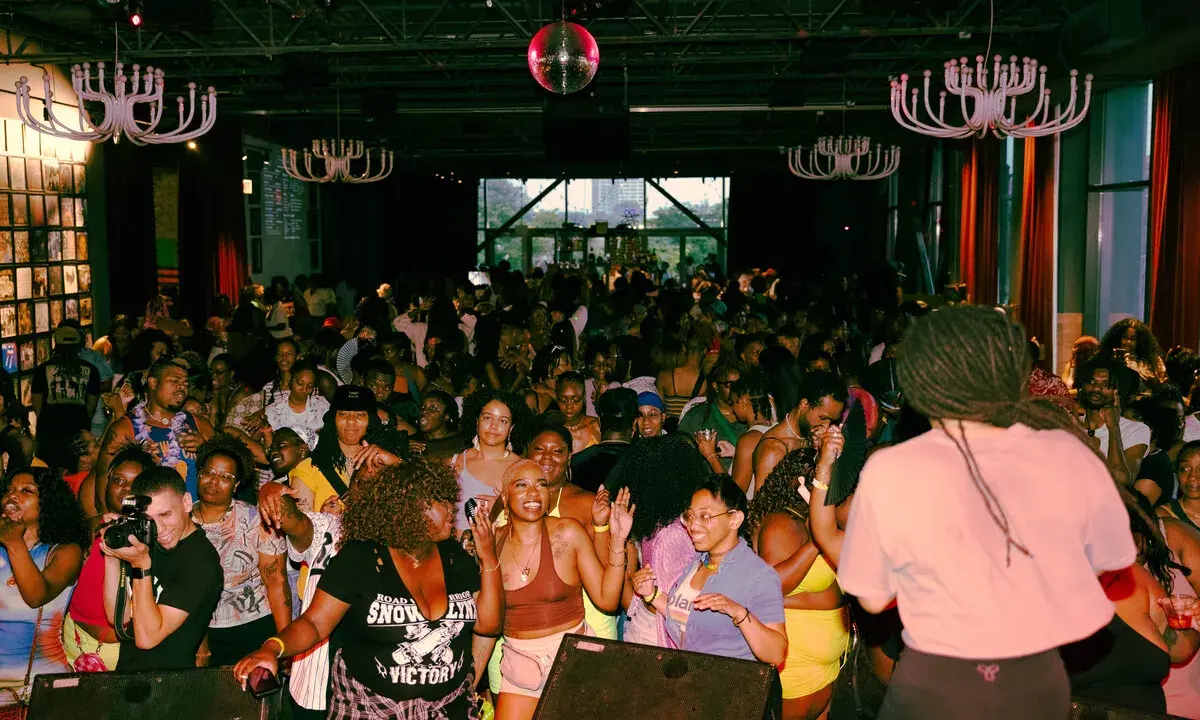 A vibrant crowd dances at a lively event, possibly one of the best gay bars in Chicago, under a disco ball and ornate chandeliers.