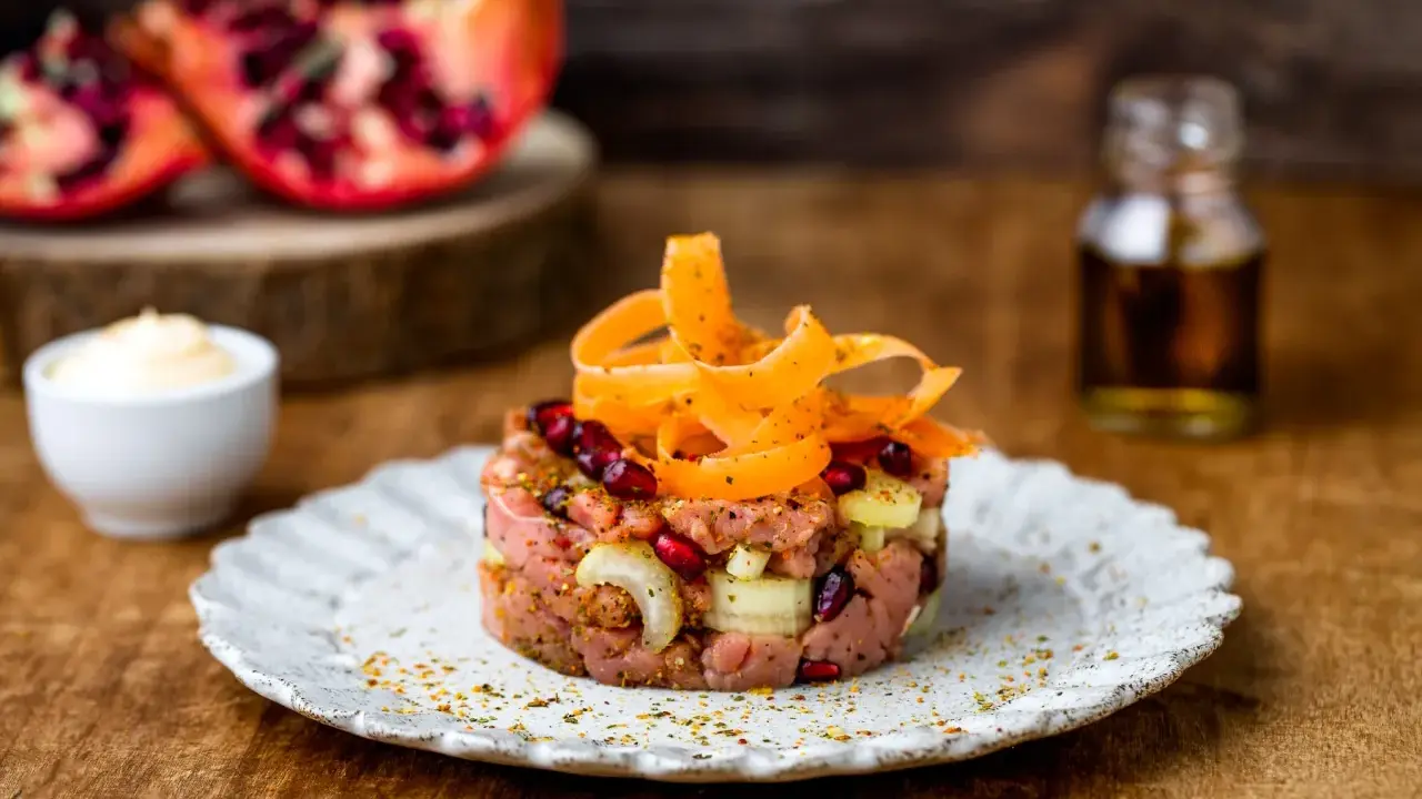 Deliziosa tartare di manzo con melograno, cipolla e carote a spirale, servita su un piatto rustico.