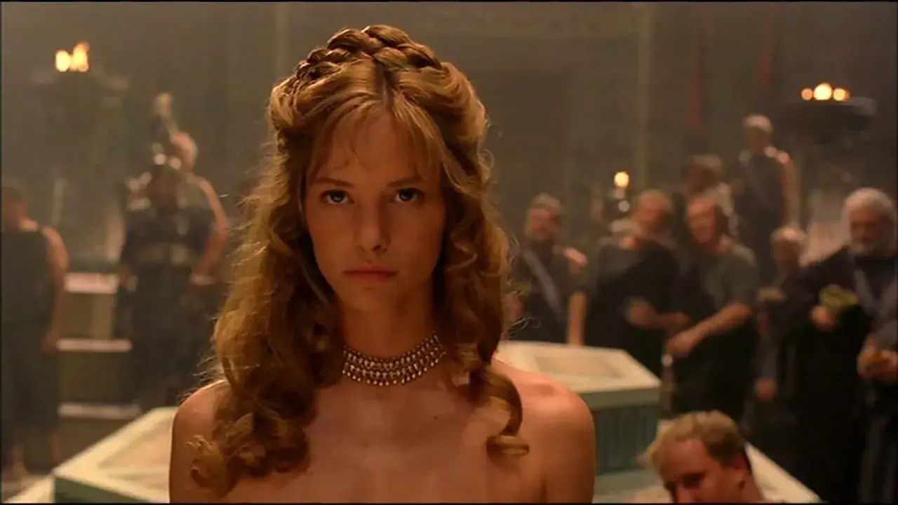 Die schöne Helena, Menelaos' Frau, blickt ernst in die Menge. Ihr Haar ist kunstvoll geflochten, ein goldenes Halsband schmückt ihren Hals.