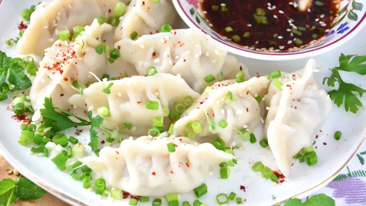 Pierożki gyoza, posypane szczypiorkiem i sezamem, podane z sosem.