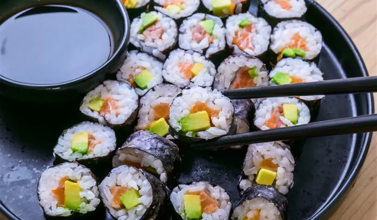 Un plato negro lleno de maki sushi de salmón y aguacate, listo para ser disfrutado con salsa de soja.