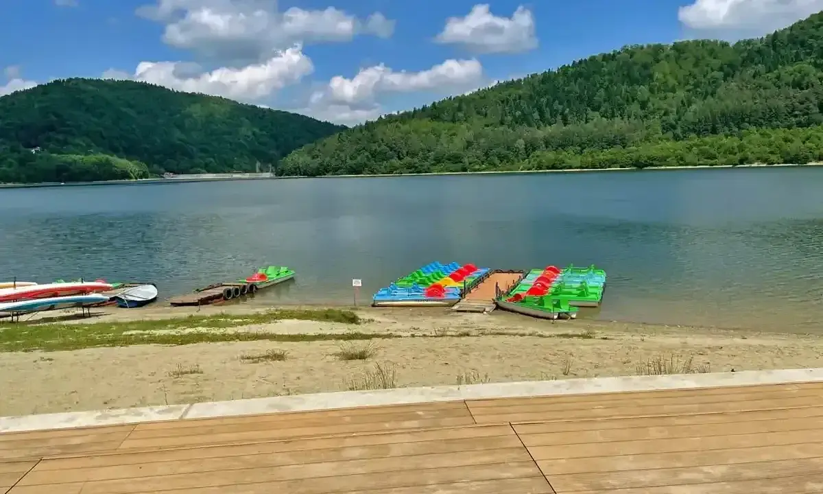 Jezioro Klimkowskie plaża z kolorowymi rowerami wodnymi i kajakami, otoczona zielonymi wzgórzami.