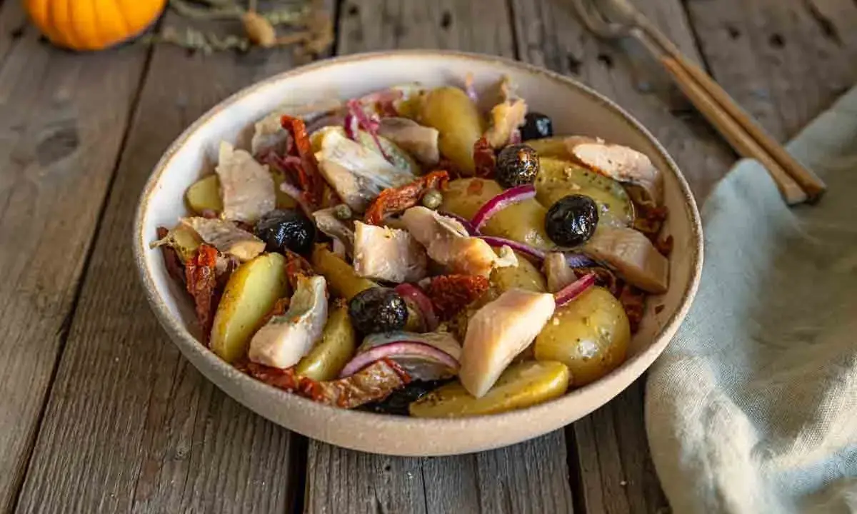 Salade de pommes de terre et hareng, garnie d'olives noires, de tomates séchées et d'oignons rouges. Un plat savoureux et coloré.
