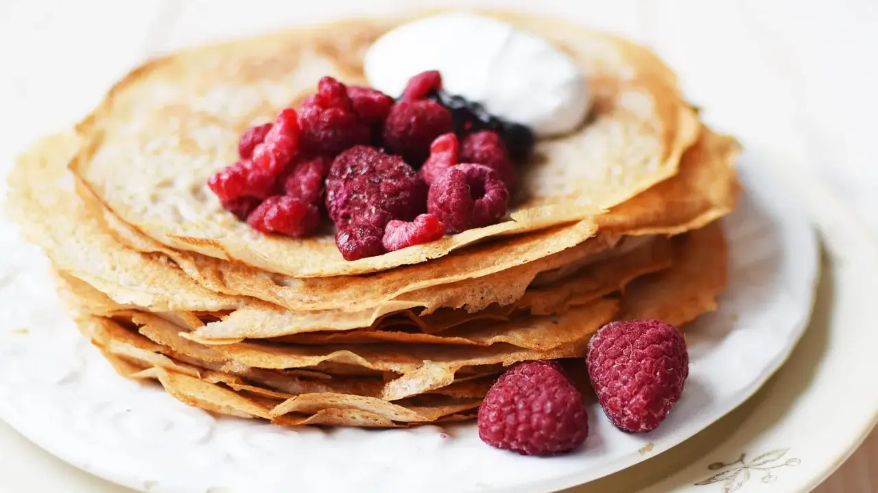 En hög med glutenfria pannkakor toppas med färska hallon och en klick grädde. Perfekt för en frukost eller fika.