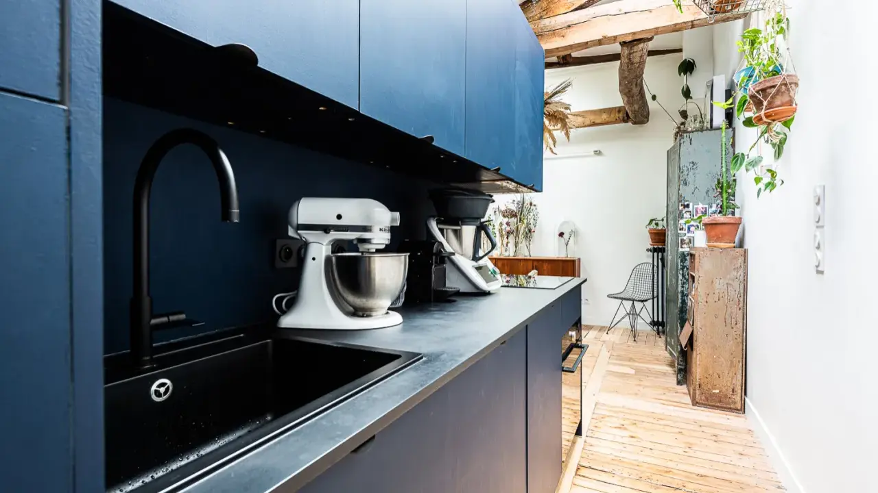 Cuisine moderne avec armoires bleues, évier noir et robot pâtissier. L'entrée de la maison donne directement dans cette pièce fonctionnelle et stylée.