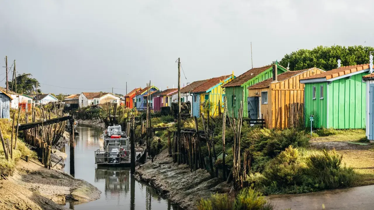 Cabanes colorées alignées le long d'un canal, un bateau amarré. Un charmant port sur l'Île d'Oléron.