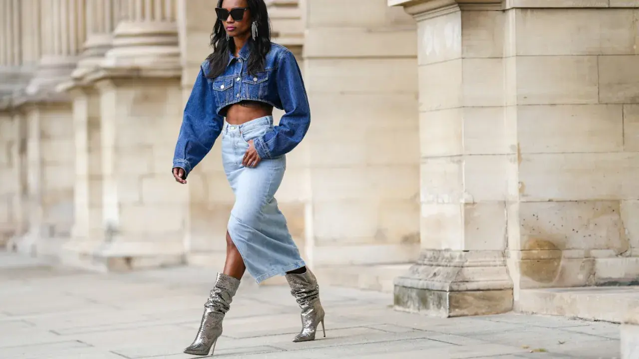 Modella con giacca di jeans corta e gonna lunga, stivali argento scintillanti. Un look che ricorda la moda degli anni '80.