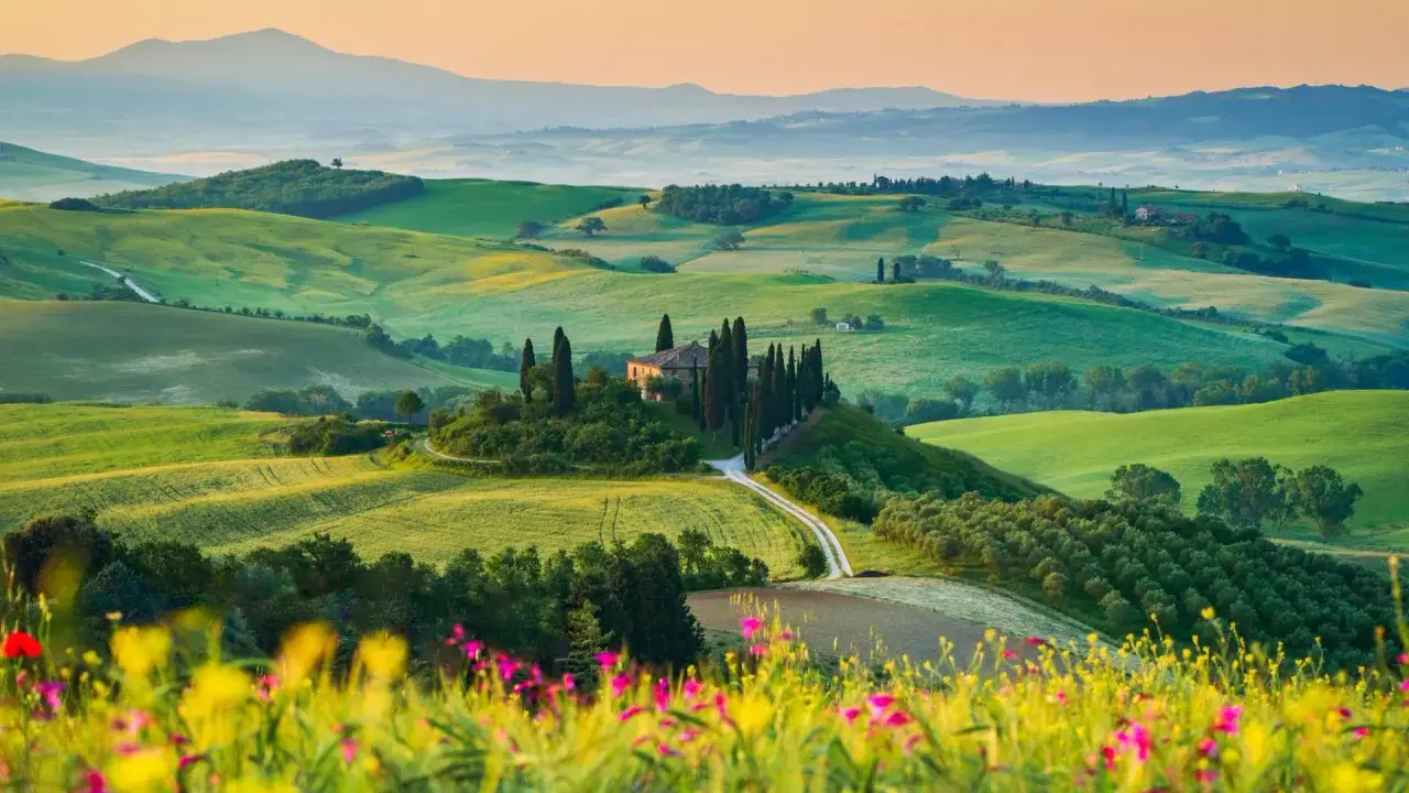 Un casale solitario su una collina, circondato da cipressi e dolci colline verdi, un sogno per un tour della Toscana.