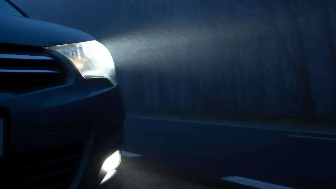 El alumbrado de posición de un coche ilumina la niebla en una carretera oscura.