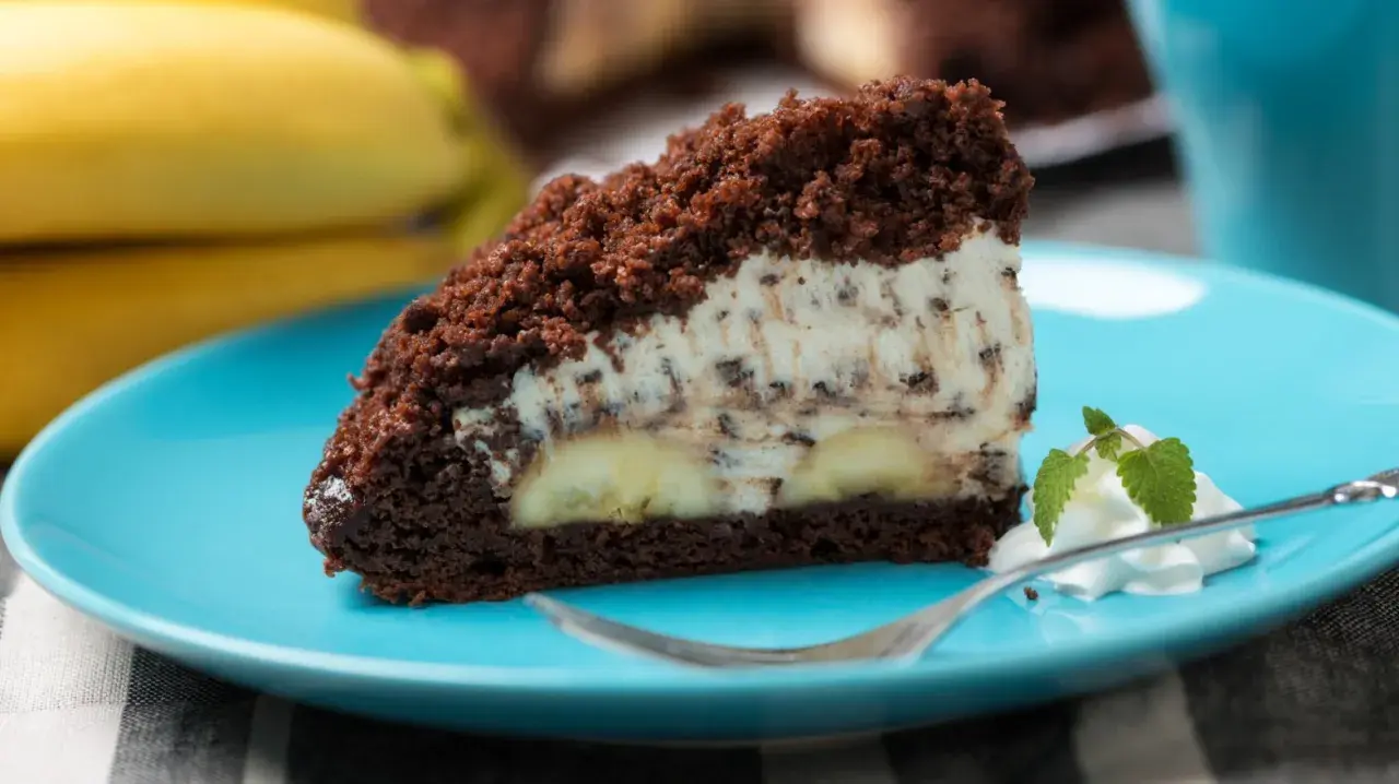 Ein Stück saftiger Maulwurfkuchen vom Blech mit Bananen und Schokostückchen in der Creme, garniert mit Sahne und Minze.