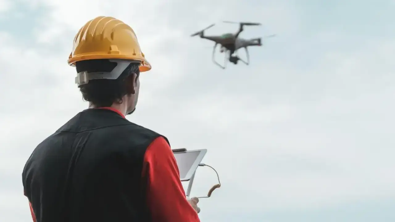 Operator drona w żółtym kasku steruje maszyną za pomocą tabletu.