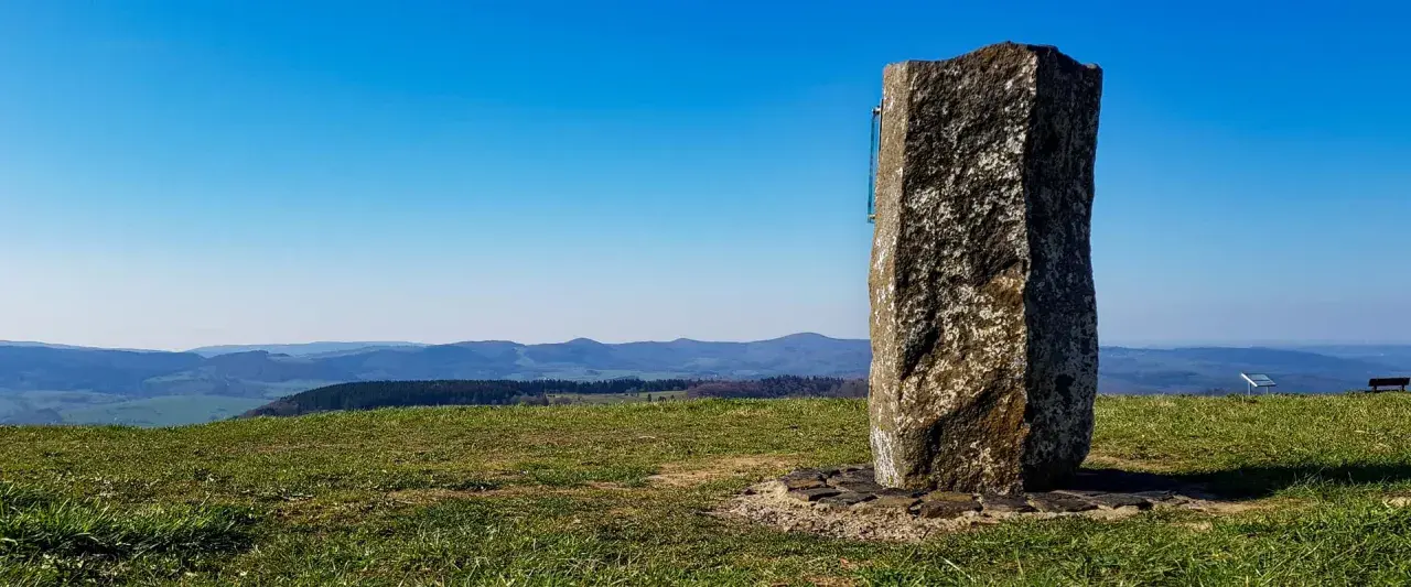 Steinerner Gedenkstein auf der Wasserkuppe mit Blick über Hügel und Täler.