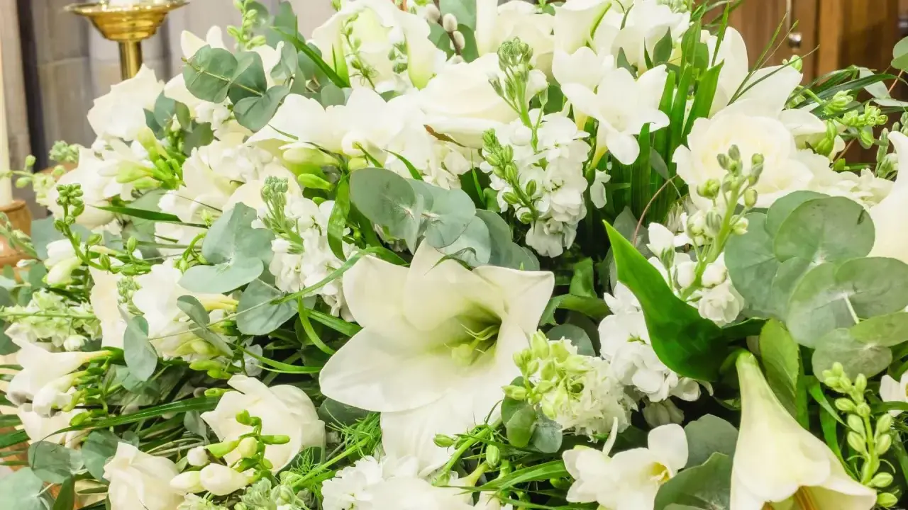 Piękna, biała wiązanka kwiatów z liliami, różami i zielonymi liśćmi.
