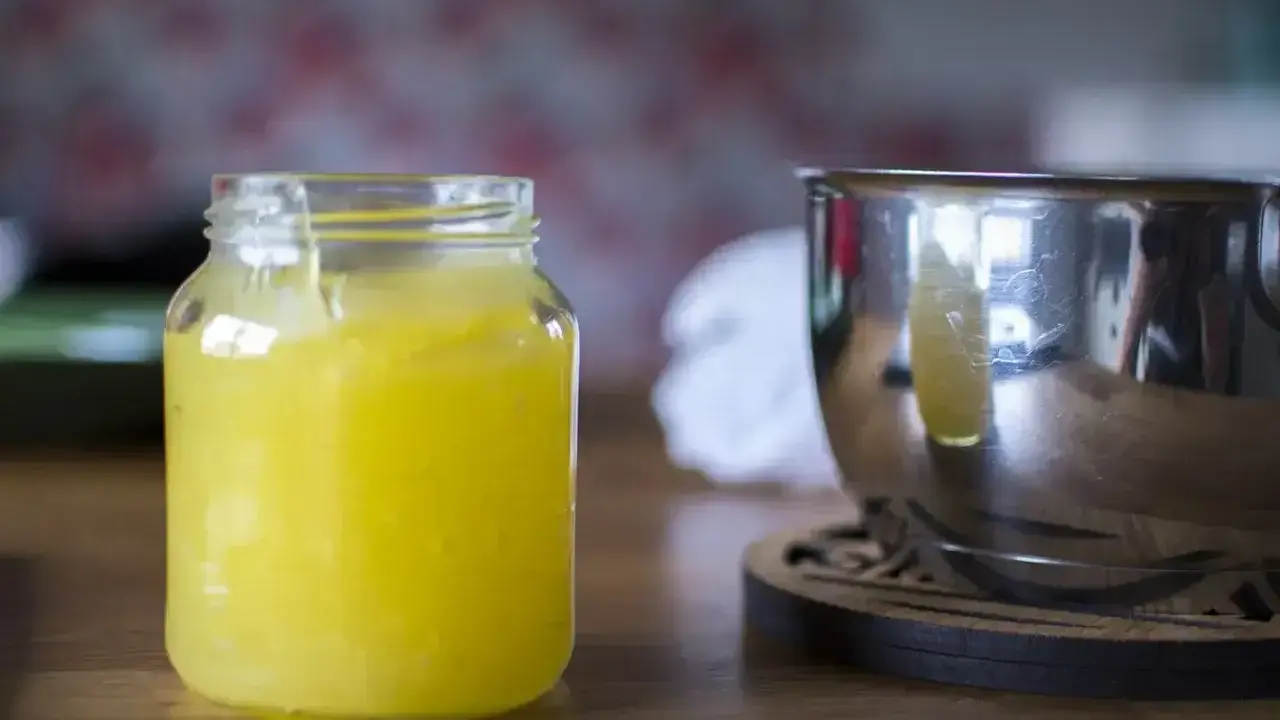 En burk med hemgjord lemon curd står bredvid en metallskål.