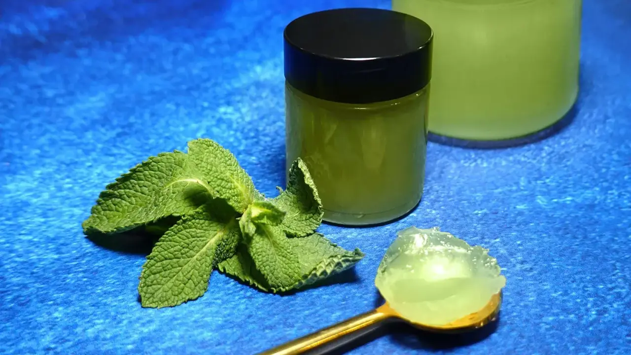 Une cuillère dorée présente une portion de gelée de menthe fraîche. À côté, un pot fermé et un autre ouvert contiennent cette même gelée verte et rafraîchissante.