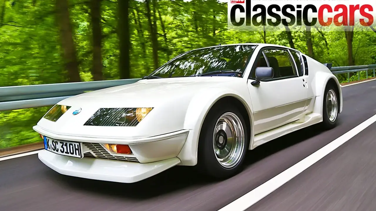 Weißer Renault Alpine A310 fährt auf einer Straße durch einen grünen Wald.