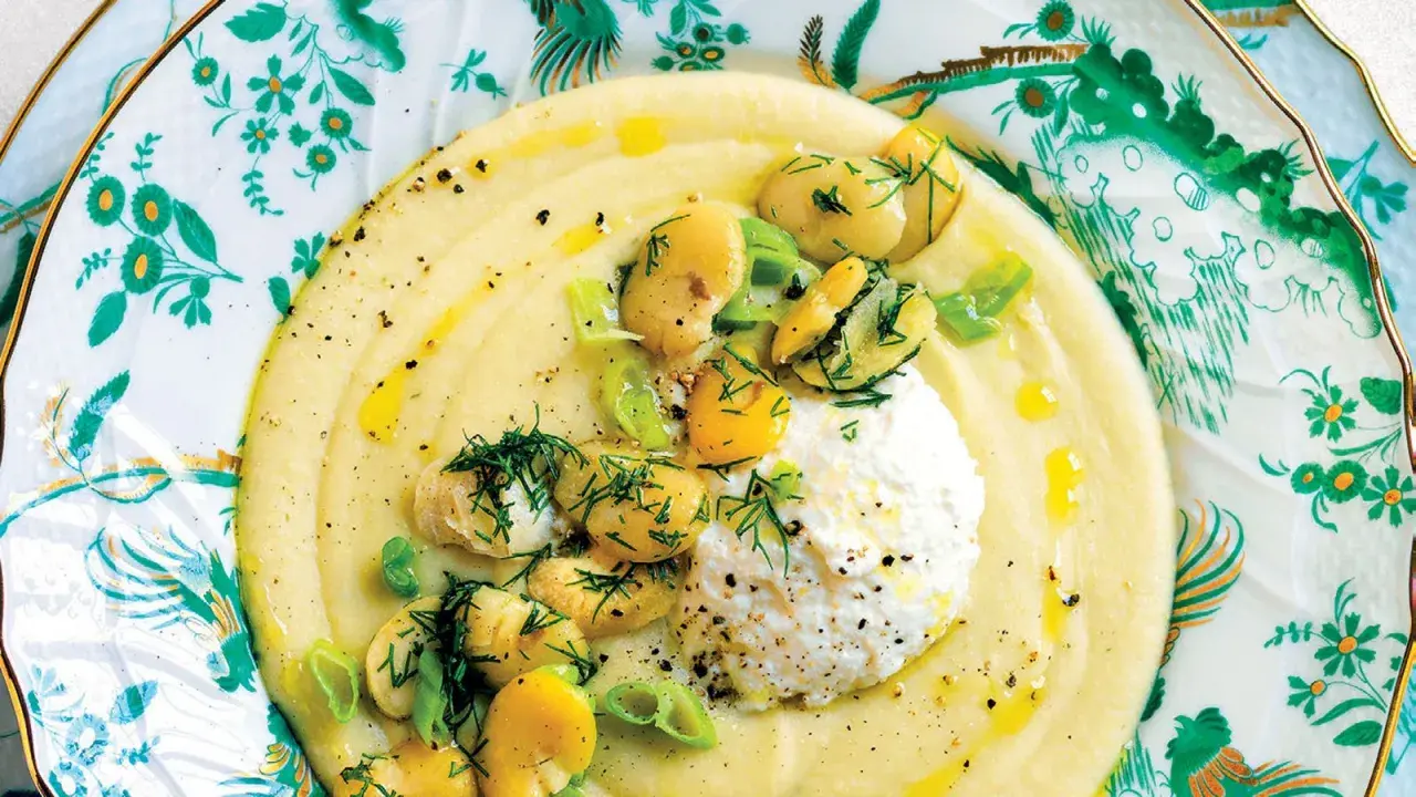 Macco di fave fresche cremoso, guarnito con fave intere, ricotta fresca e aneto, servito su un piatto decorato.