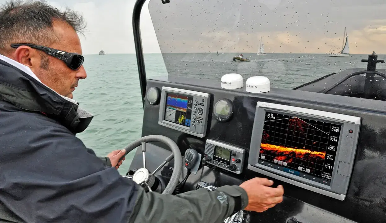 Un homme navigue, consultant un écran de sonar affichant des données sous-marines.