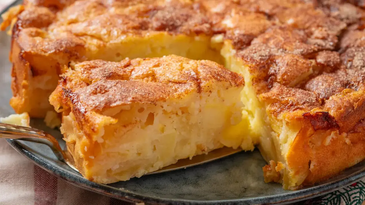 Ein goldbrauner Apfelkuchen mit Zimtstreuseln, der Lust auf tolle Apfelkuchen Rezepte macht. Ein Stück wird gerade herausgehoben.