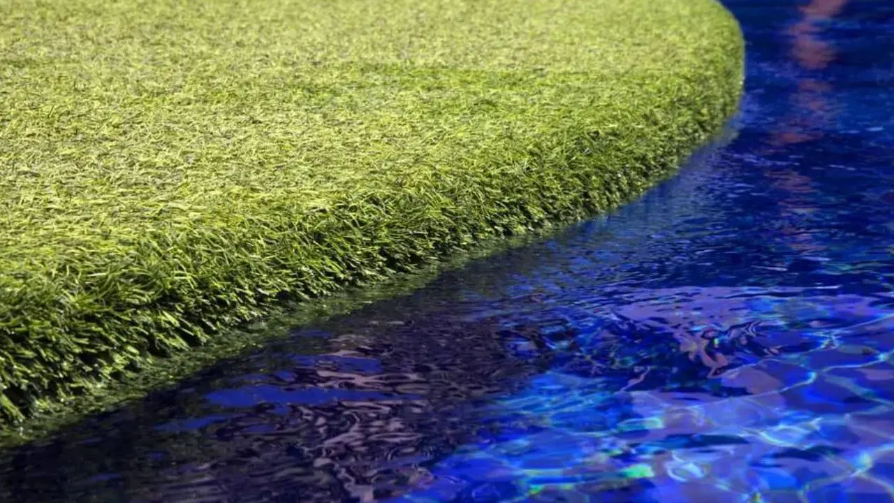 A vibrant green artificial grass island floats in a bright blue pool. The question of will chlorine kill grass is answered by this synthetic turf, unaffected by the water.