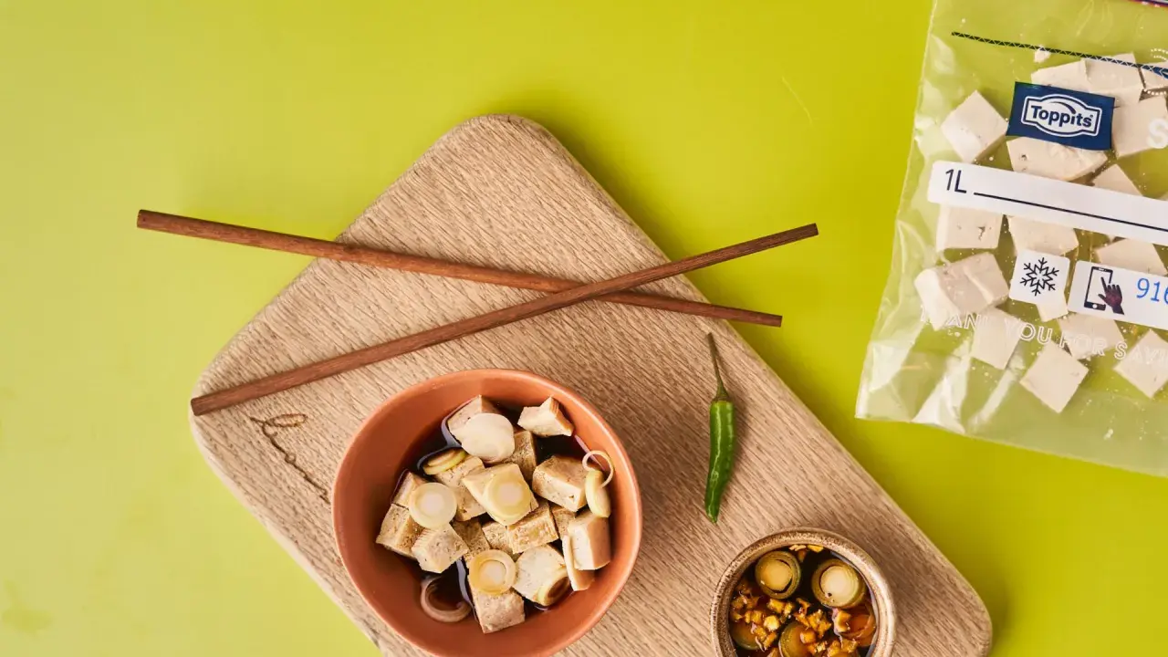 Vorbereitung für tofu einfrieren: gewürfelter Tofu in Schüssel mit Soße, daneben Stäbchen, Chili und ein Gefrierbeutel mit Tofuwürfeln.