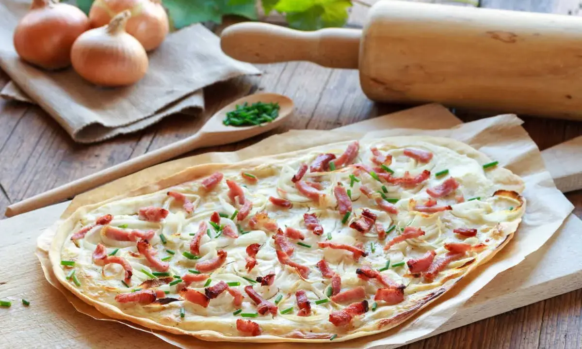 Flammekueche prête à être dégustée, avec ses oignons, lardons et ciboulette. Une recette facile pour un repas convivial.