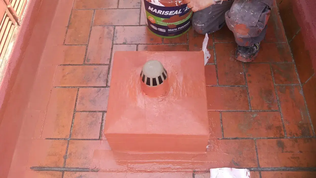 Persona aplica pintura para impermeabilizar terraza. Cubeta de Mariseal y desagüe en el centro.