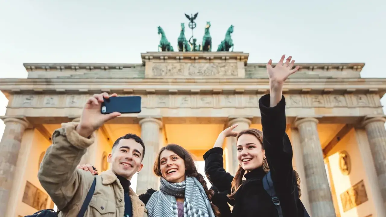 Tre glada vänner tar en selfie framför Brandenburger Tor, en ikonisk sevärdhet att se i Berlin.