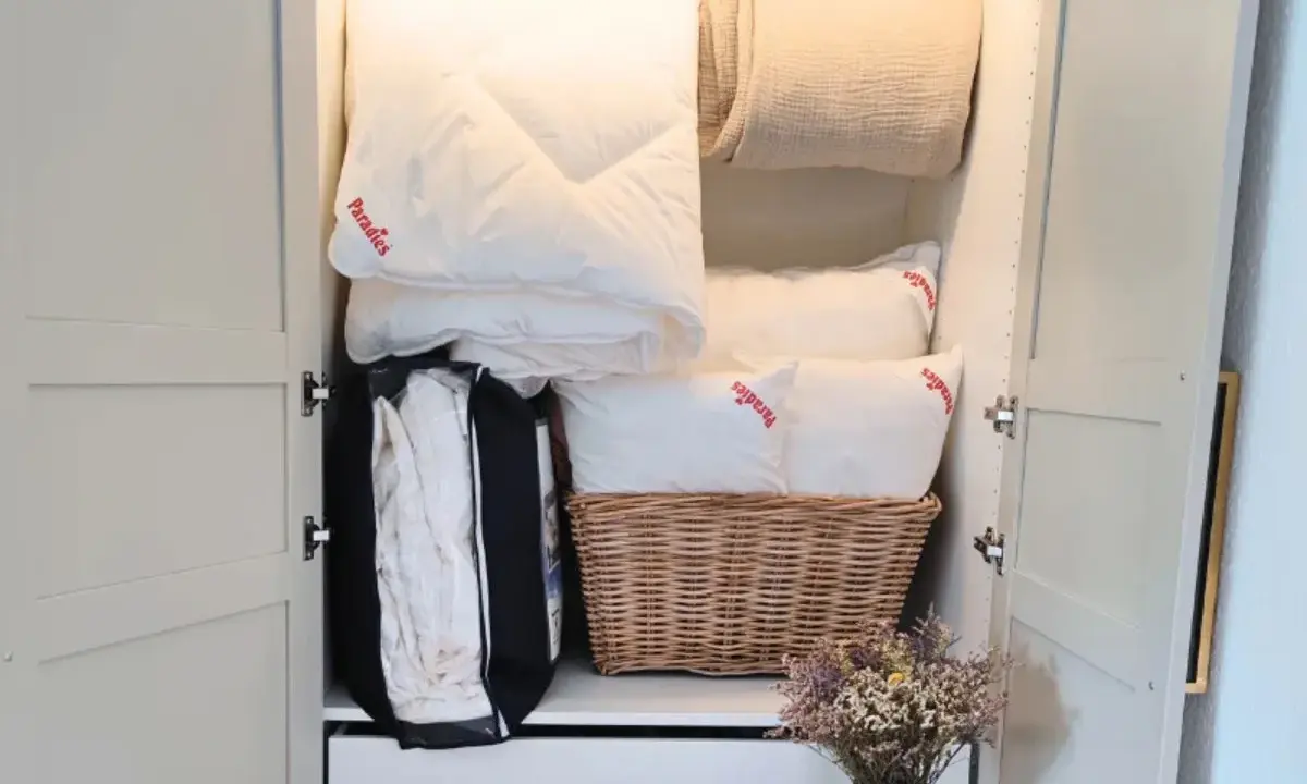 Ordentlich verstaut: weiße Bettdecke falten und Kissen im Schrank, daneben eine Decke und ein Korb mit Bettzeug.