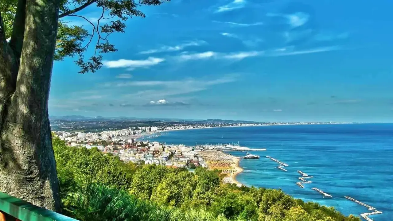 Vista panoramica della Riviera Romagnola con mare azzurro, spiagge affollate e una città costiera. Ideale per il turismo.