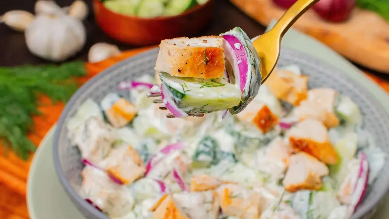 Ein Löffel mit einem Stück Hähnchen, Gurke und roter Zwiebel, bereit, in einen cremigen Salat zu tauchen. Perfekt für proteinreiche Salate!