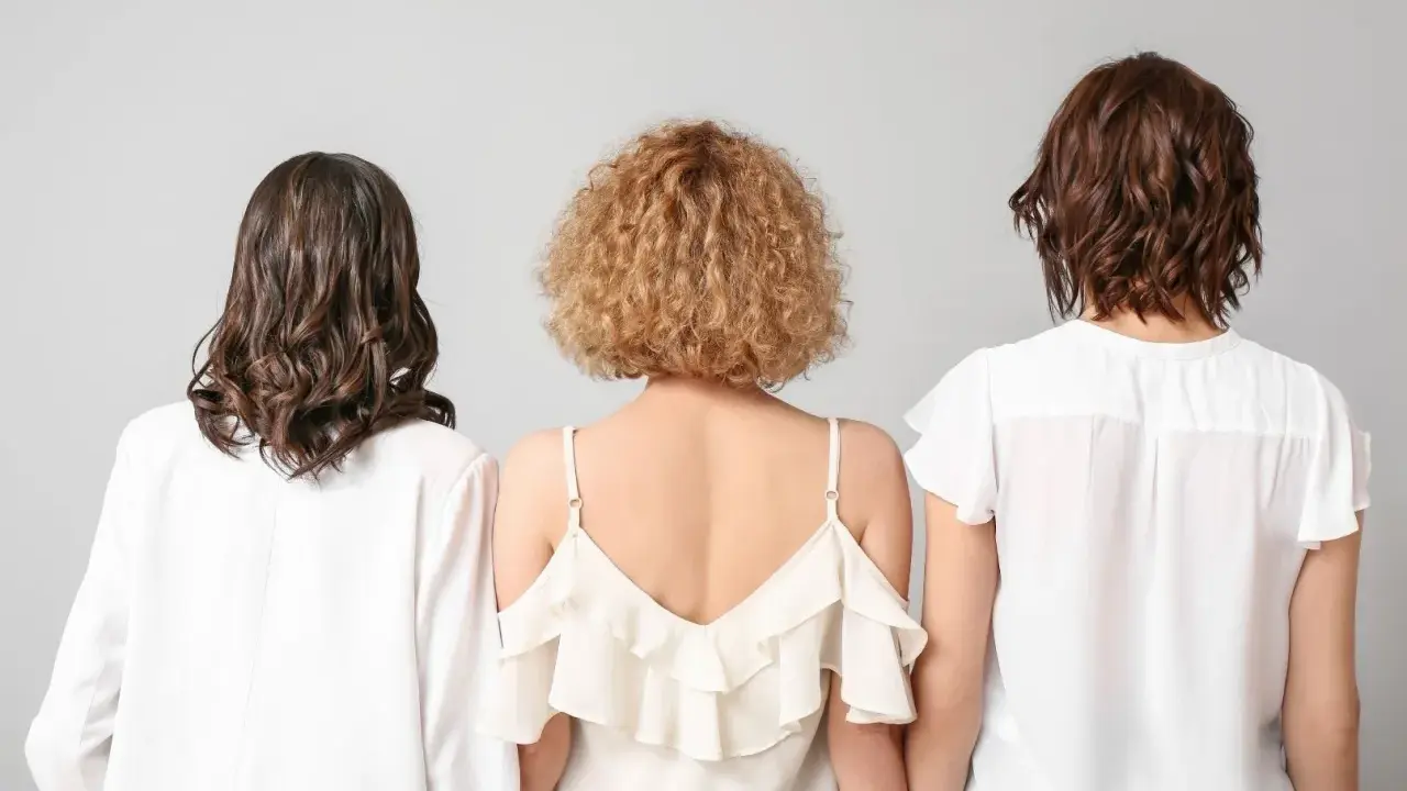 Trzy kobiety z tyłu. Jedna ma falowane, ciemne włosy, druga krótkie, kręcone blond włosy w stylu boho, trzecia falowane, brązowe włosy.