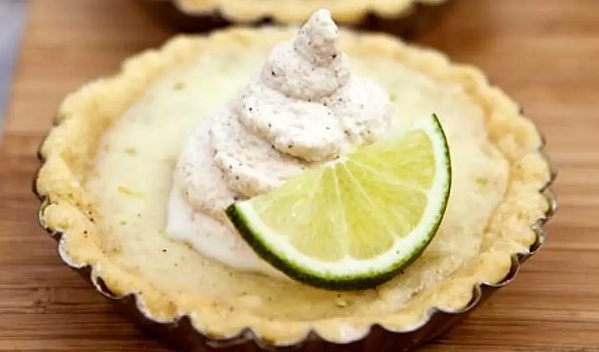 En liten key lime pie med en virvel av gräddig topping och en limeklyfta.