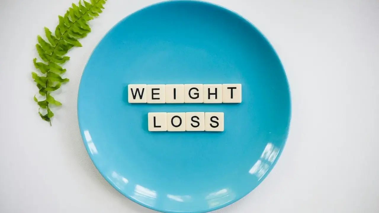 Niebieski talerz z literami tworzącymi napis "WEIGHT LOSS" i gałązką paproci. Pytanie o makro na redukcji?