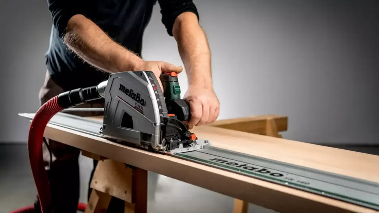 Main d'un artisan guidant une scie circulaire sur un rail pour une coupe précise sur une planche de bois.