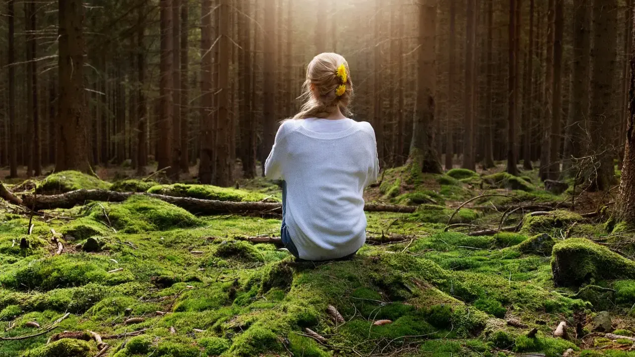 Frau sitzt im Wald auf moosbewachsenem Boden, sucht Ruhe, wenn sie immer gestresst und genervt ist.