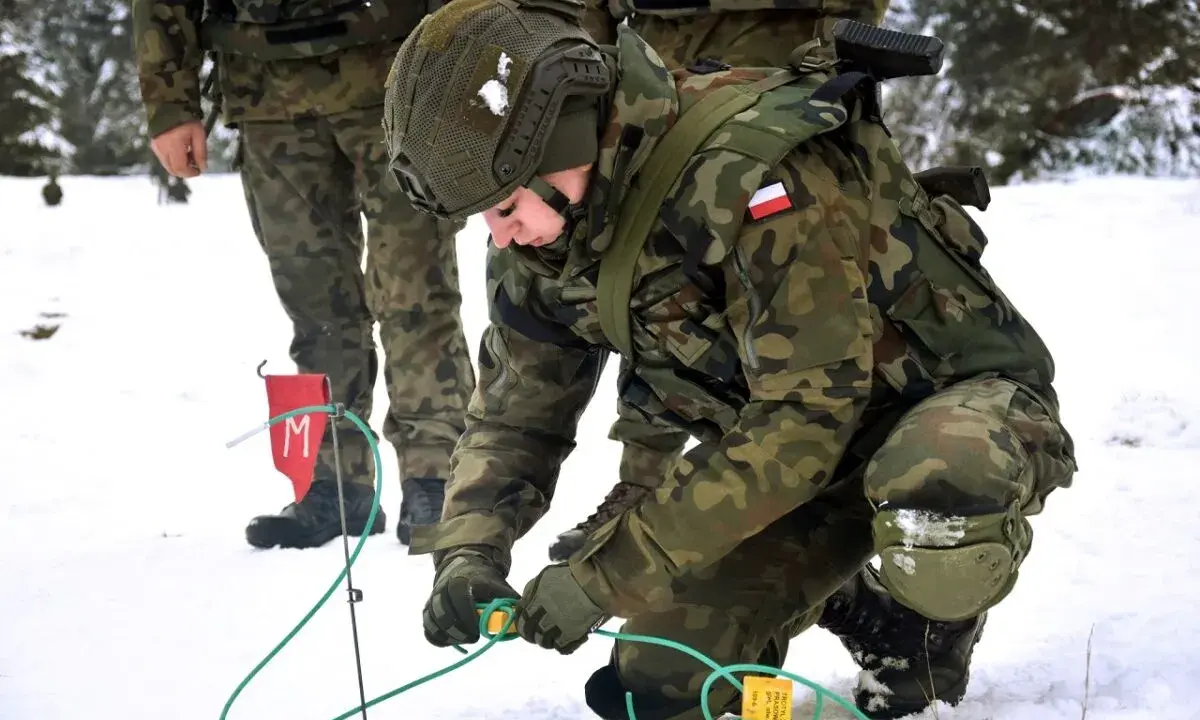 Żołnierz w zimowym kamuflażu, kto to saper, ostrożnie pracuje z przewodami i flagą z literą "M".