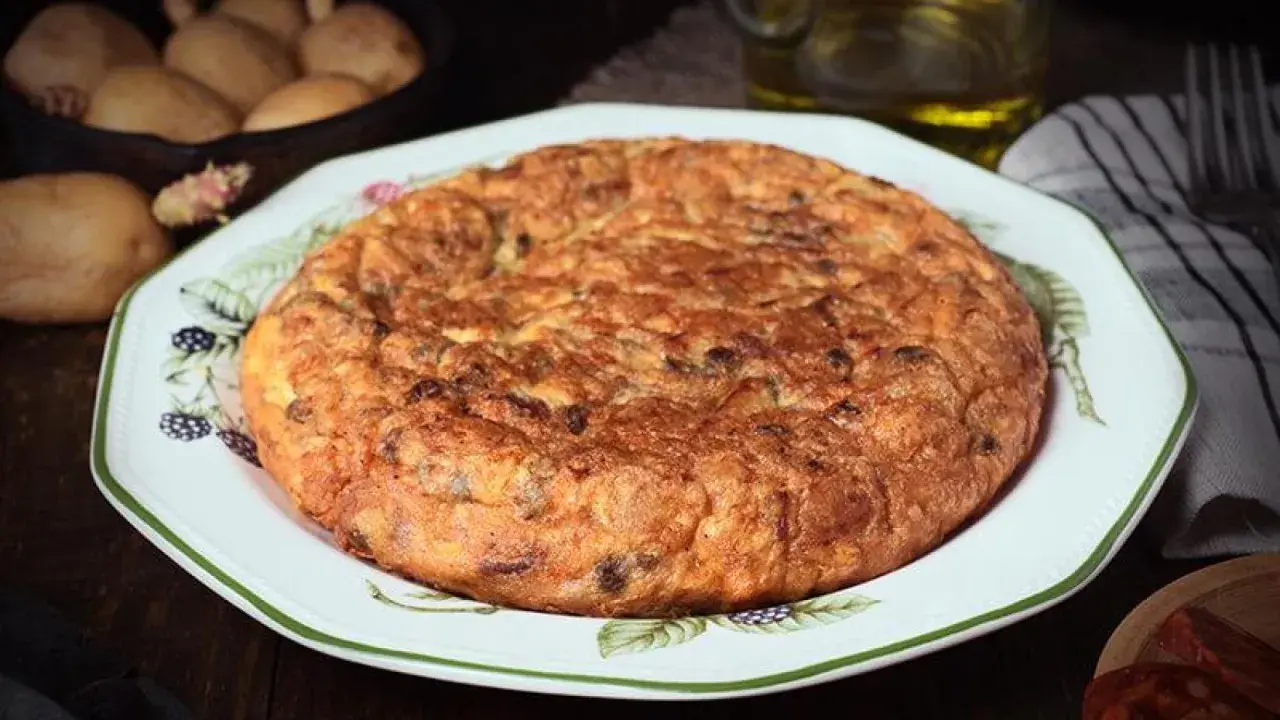 Tortilla española, un clásico de la comida típica de Granada, servida en un plato decorado. Patatas y aceite en el fondo.