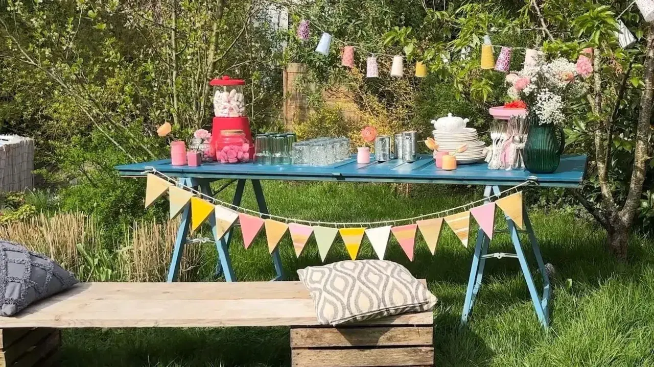 Une table bleue dressée pour une deco garden party à faire soi même, avec guirlandes, bonbons et fleurs.