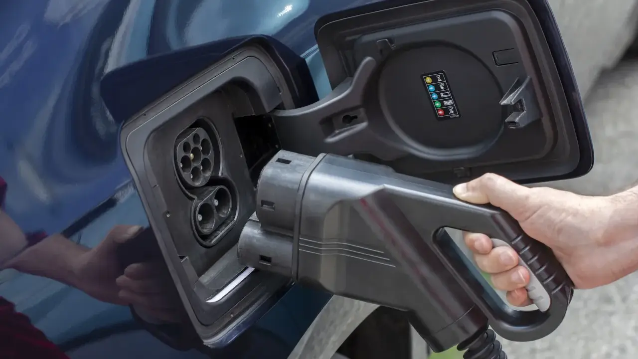 Mano insertando cargador en coche eléctrico. Averigua cuanto tarda en cargar un coche eléctrico en casa.