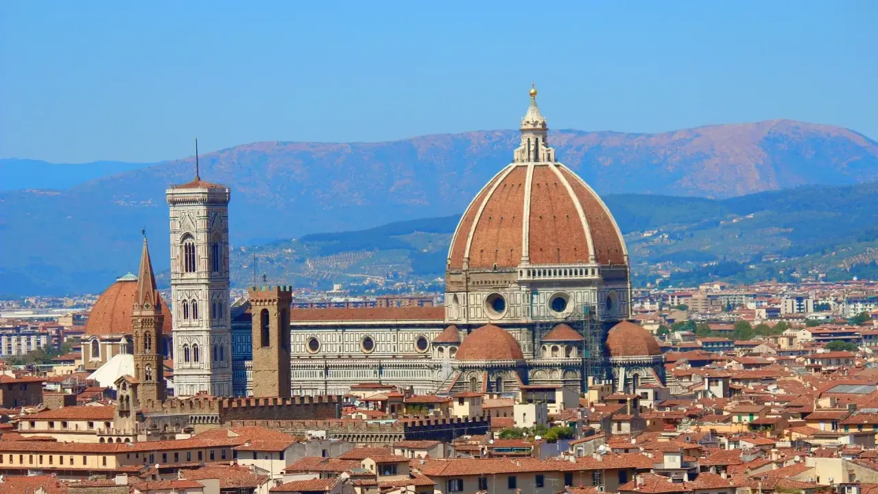 Vue panoramique de Florence avec le **dôme de Brunelleschi** dominant la ville, sous un ciel bleu clair.