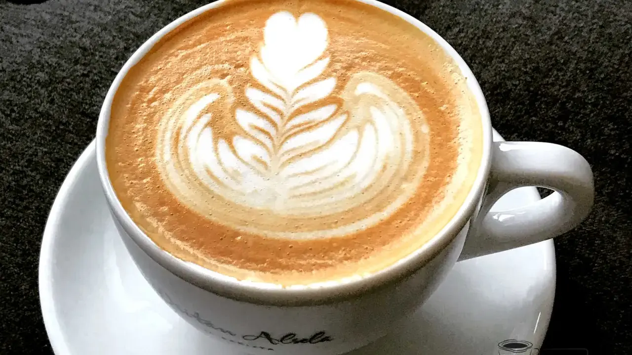 Eine Tasse Cappuccino mit kunstvoller Barista Art, die ein Herz und Blätter zeigt.