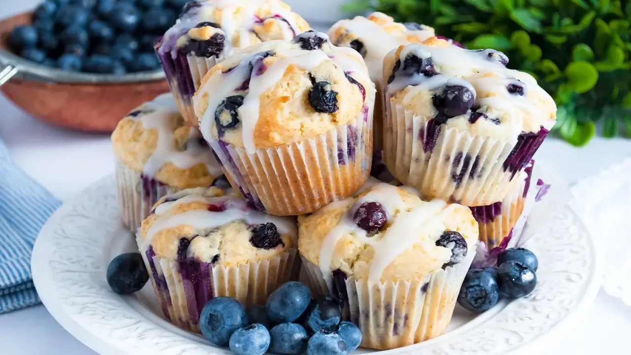 Stosik pysznych muffinek z borówkami, polanych lukrem, ozdobiony świeżymi owocami.