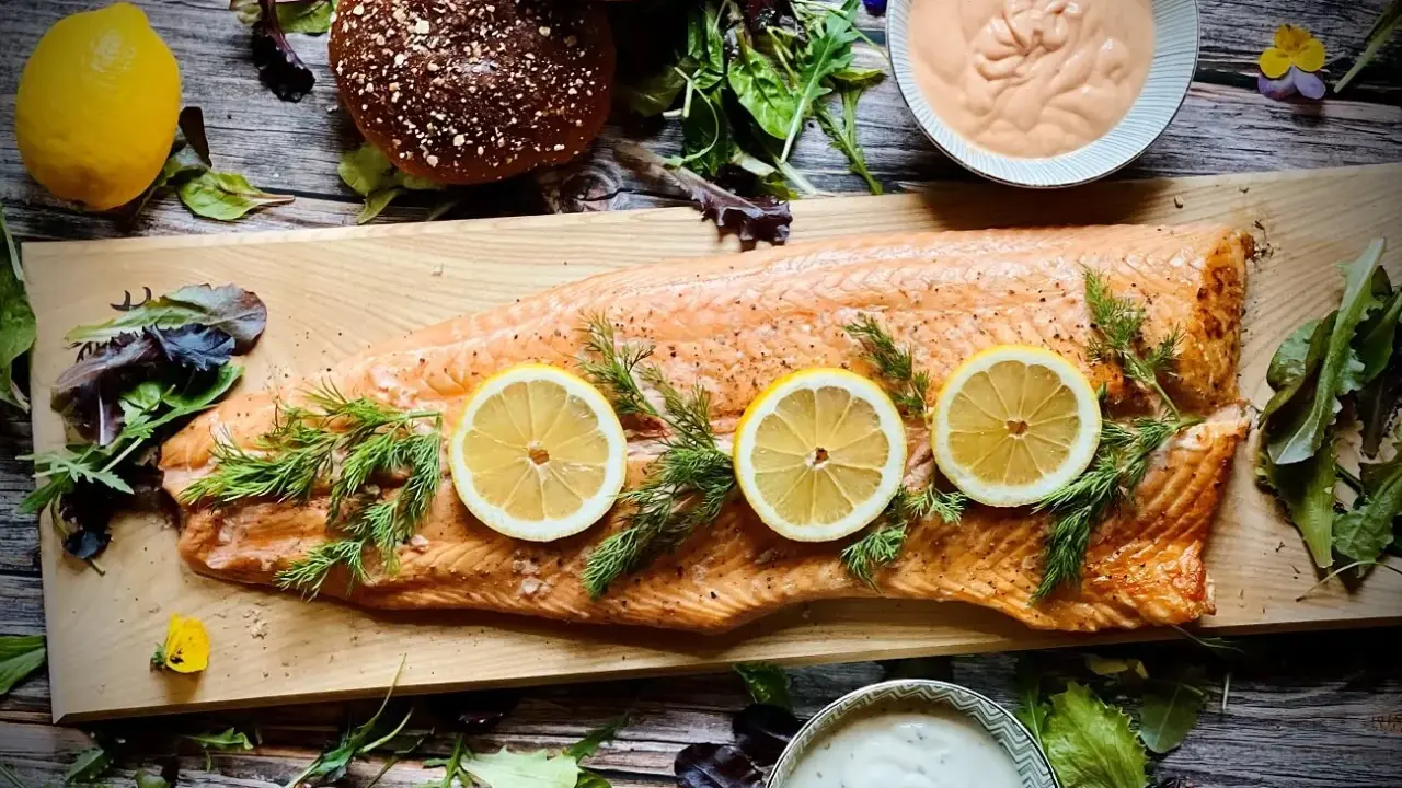 Flammlachs mit Zitronenscheiben und Dill, serviert mit cremigen Dips und frischem Salat als Beilagen.