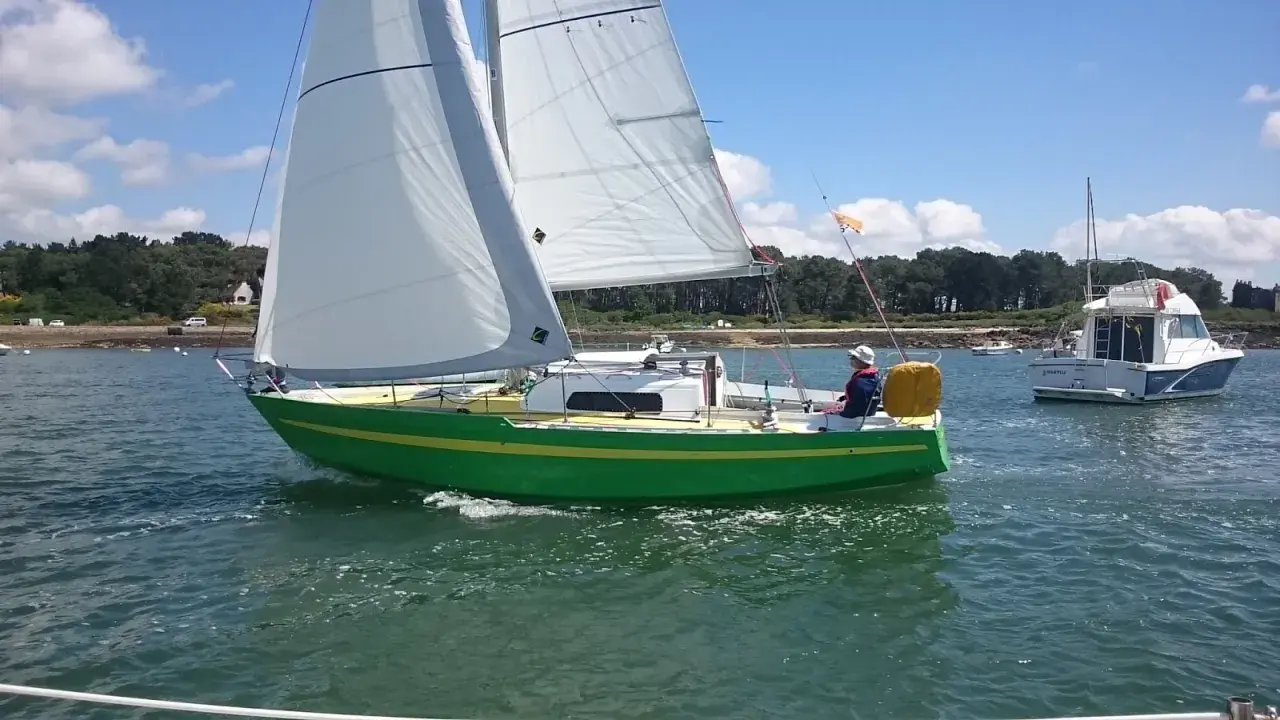 Un voilier vert vif navigue sur l'eau, avec un autre bateau à moteur en arrière-plan. Une belle journée pour une croisière, peut-être avec une dégustation d'armagnac à bord de ce bateau.
