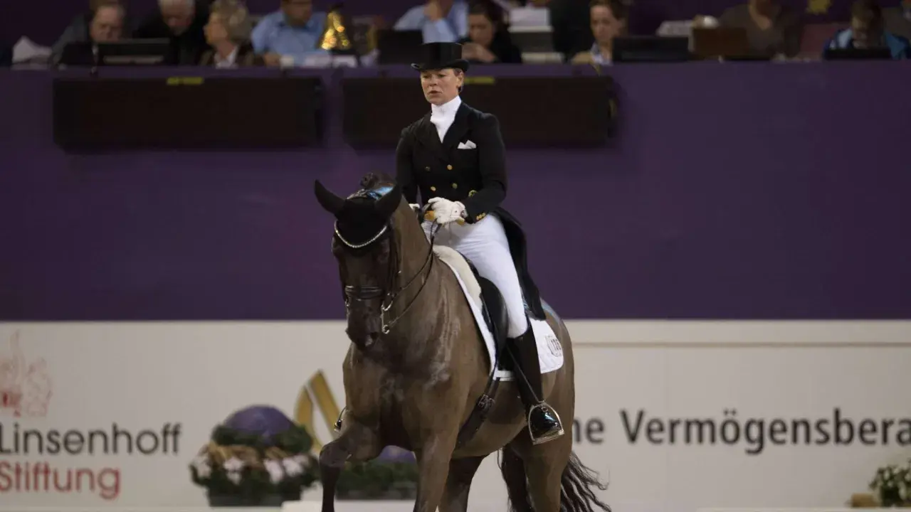 Kira Wulferding im Dressurstall, elegant in Frack und Zylinder, präsentiert ihr Pferd in einer anspruchsvollen Lektion.