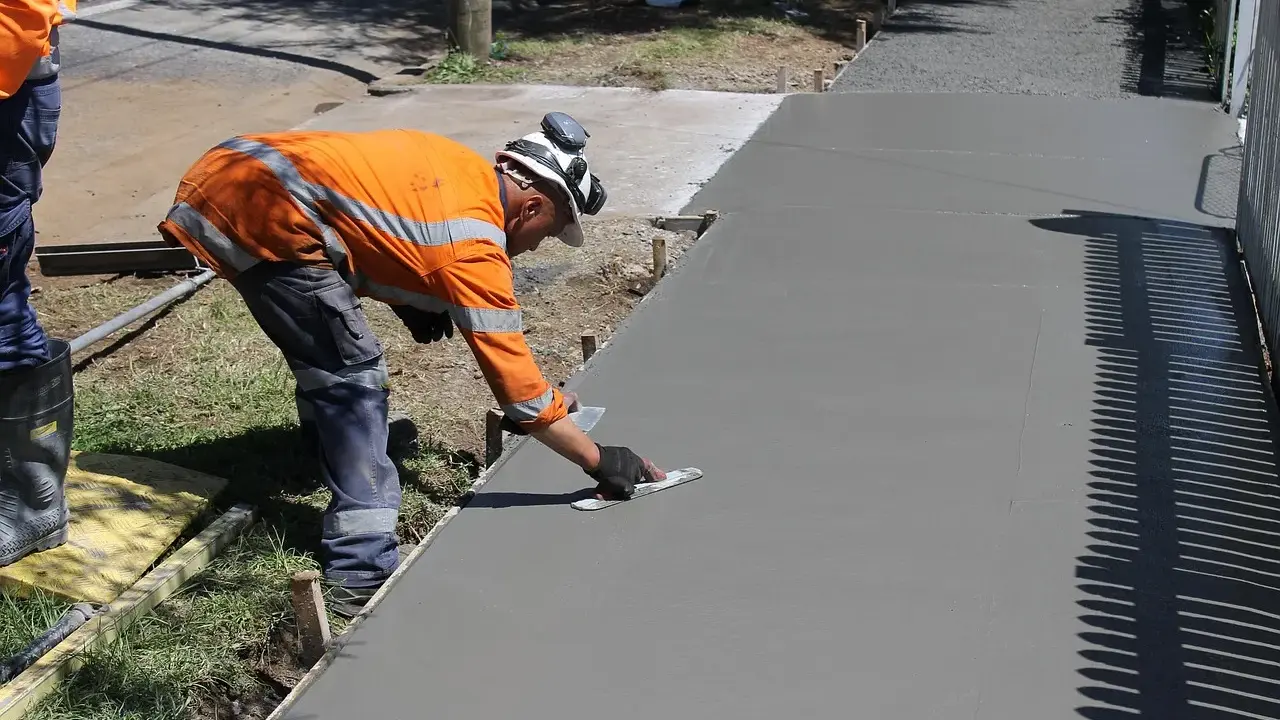Robotnik wygładza świeży beton, zastanawiając się, ile kosztuje kubik betonu na nową ścieżkę.