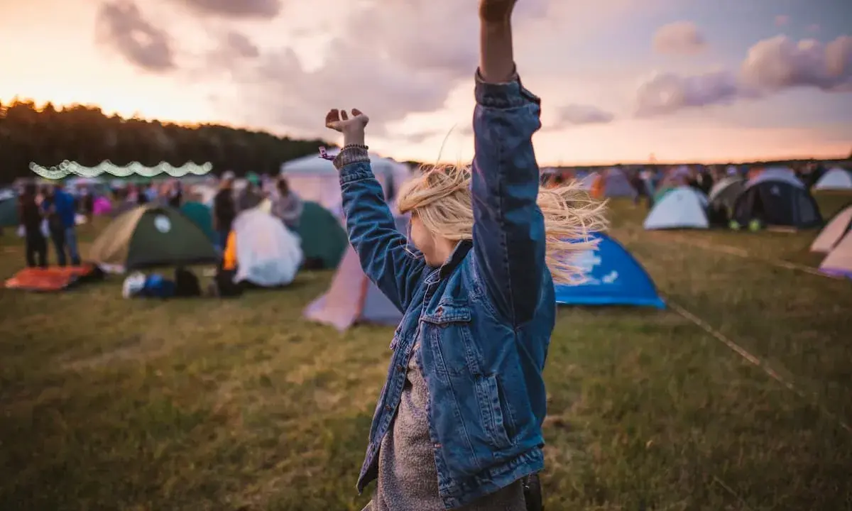 Ragazza con le braccia alzate in un campo di tende, immersa nell'atmosfera di uno dei festival techno più famosi.